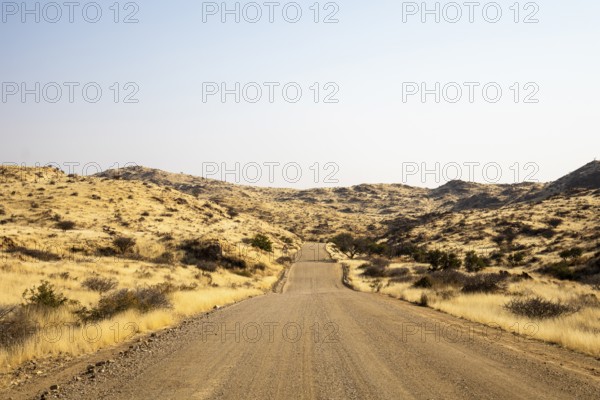 A road Spreetshoogte Pass in Namibia, with a gravel road winding through golden grassland and rocky hills under a bright, clear sky