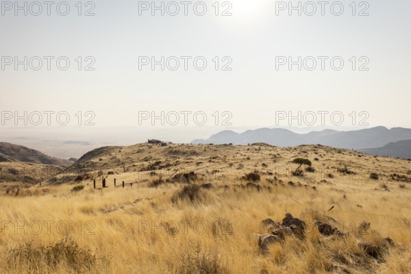 A picnic spot overlooks the vast Namib Desert from Spreetshoogte Pass, with hazy plains, rugged mountains, and a lone house on the ridge under the bright sky
