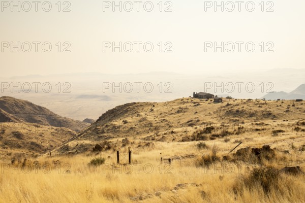 A picnic spot overlooks the vast Namib Desert from Spreetshoogte Pass, with hazy plains, rugged mountains, and a lone house on the ridge under the bright sky