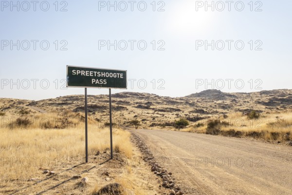 A road sign marks Spreetshoogte Pass in Namibia, with a gravel road winding through golden grassland and rocky hills under a bright, clear sky