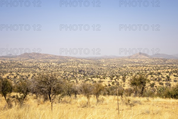 A sweeping view of Windhoek, Namibia, where a desert landscape under a clear blue sky, framed by dry hills, scattered vegetation, and distant mountains