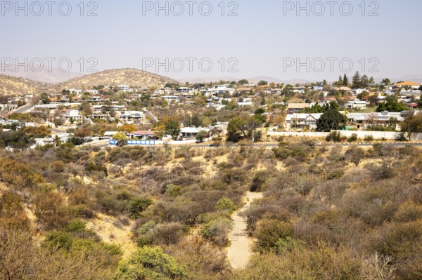 A panoramic view of Windhoek, Namibia, from the National Botanic Garden, showing the city's mix of homes, modern buildings, and a distant church framed by dry hills and mountains