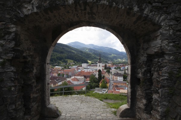 View through a stone Tor tor to a town with church tower and surrounding mountains, Bruck an der Muhr Styria Austria