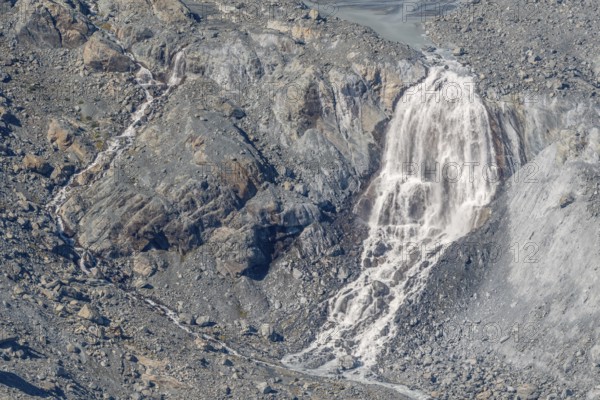 Waterfalls flow over a glacier surrounded by rocks and debris. This natural phenomenon is caused by the melting of ice, which can be observed on sunny days