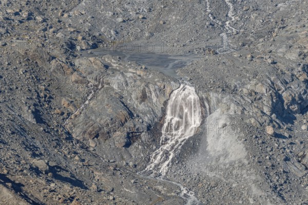 Waterfalls flow over a glacier surrounded by rocks and debris. This natural phenomenon is caused by the melting of ice, which can be observed on a sunny day. Gorner Glacier, Zermatt, Valais, Alps, Swiss