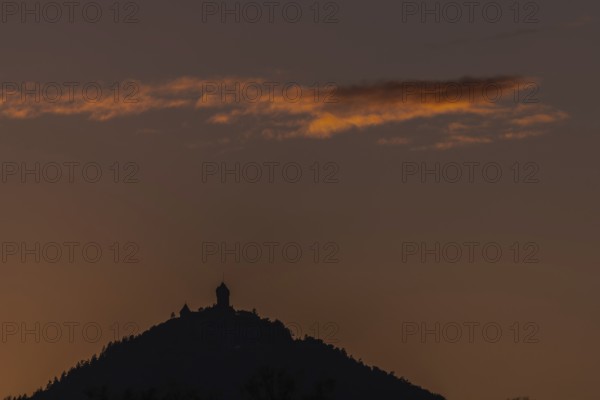 The top of the mountain is cut off against the orange-coloured sky at sunset. The soft light emphasises the silhouette of the structure at the top and creates a peaceful atmosphere. Haut-Koenigsbourg Castle, Bas rhin, Alsace, grand est, France