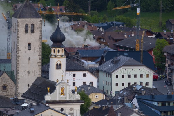 Firefighters standing on a roof fighting a fire in a house in the town centre of San Candido, San Candido, Val Pusteria, Sesto Dolomites, Dolomites, South Tyrol, Italy