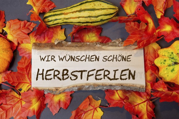 (photomontage) : Wooden sign with the inscription WIR WÜSCHEN SCHÖNE HERBSTFERIEN and autumnal decoration