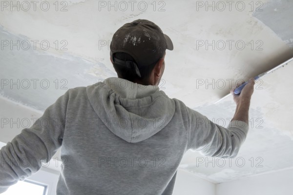 Plasterer levelling and smoothing the ceiling in the interior