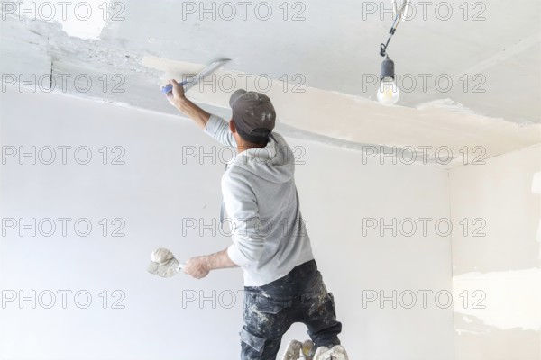 Plasterer levelling and smoothing the ceiling in the interior