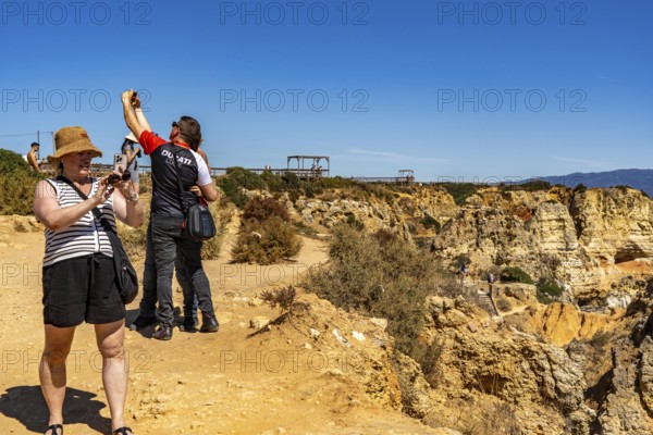 Tourists on the rocky coast of Ponta da Piedade, rugged coastal landscape, right next to Lagos city centre, in the west of the Algarve, Portugal