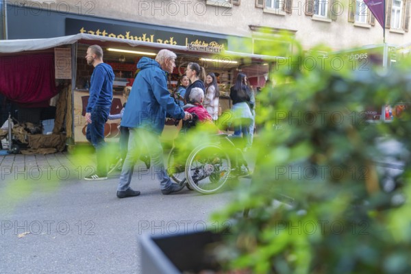 People strolling and some pushing a wheelchair along a busy market street, Sindelfingen, Böblingen district, Germany