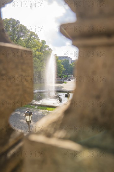 A fountain spouts water through an opening in a wall in a sunny park, Munich, Germany
