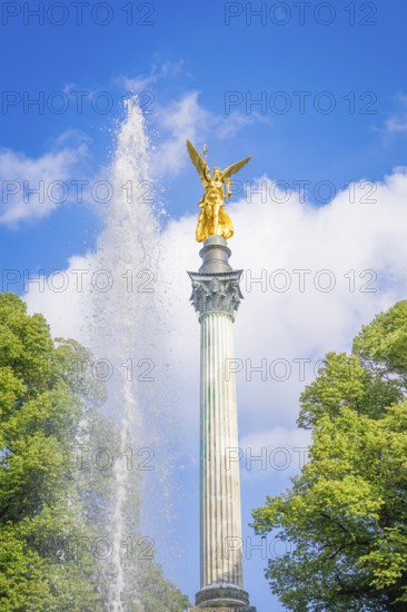Golden statue on column with fountain and trees in front of blue sky, Munich, Germany