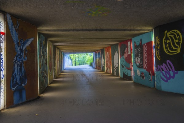 A graffiti-covered tunnel leads to a green open-air area, Munich, Germany