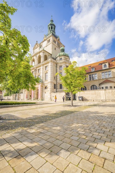 Mesmerising building surrounded by spring trees under a blue sky and paved area, Munich, Germany