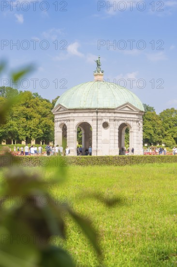 Historic pavilion with green dome in a meadow, people walking surrounded by nature, Munich, Germany
