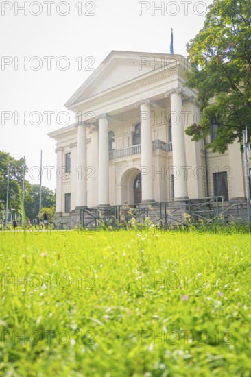 Building with white columns and large windows on a green lawn on a sunny day, Munich, Germany