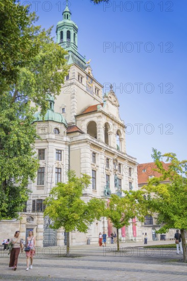 Impressive historic building with green towers and trees, people strolling by, Munich, Germany