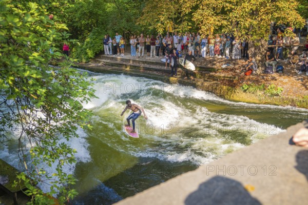 Surfers riding a powerful river wave, watched by a crowd on the shore, Munich, Germany