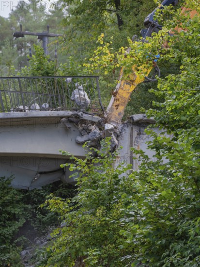 An excavator working on the end of a bridge, surrounded by dense greenery, bridge demolition, Calw, Germany