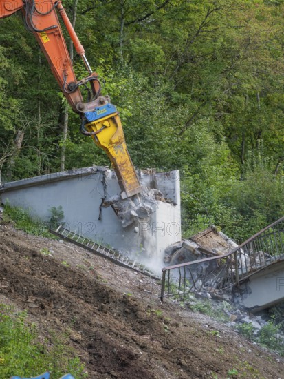 An excavator smashes concrete, dust rises, railings come loose, bridge demolition, Calw, Germany