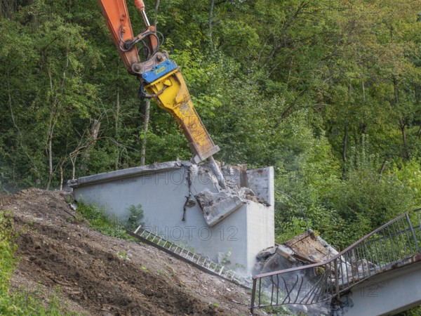 An excavator destroys a concrete wall on a slope, remains of a ladder visible, bridge demolition, Calw, Germany