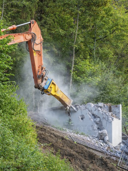 An excavator breaks a concrete wall in a green environment, dust rises, bridge demolition, Calw, Germany