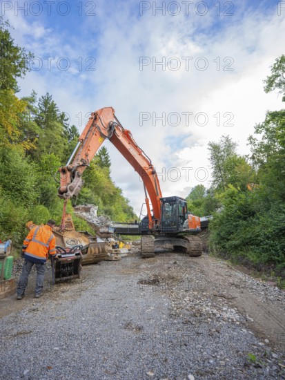 A worker and an excavator carry out work on a road covered with gravel, bridge demolition, Calw, Germany