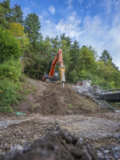 An excavator lifts earth on a slope in a forest under a blue sky, bridge demolition, Calw, Germany