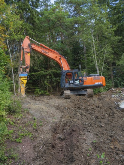 An orange excavator working on a wooded slope, bridge demolition, Calw, Germany