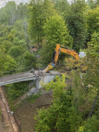 Excavator tears down part of a bridge in a green forest, an empty path runs underneath, bridge demolition, Calw, Germany