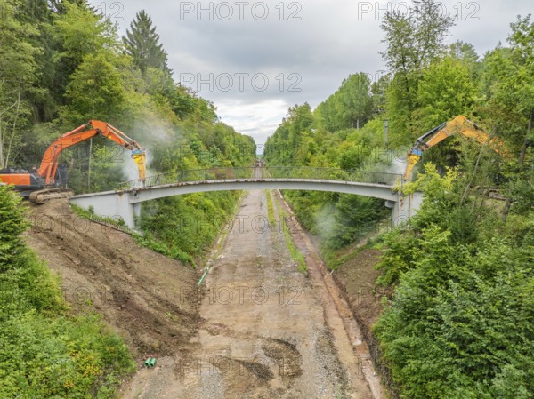 Two excavators demolishing a bridge over a forest path, surrounded by dense vegetation, bridge demolition, Calw, Germany