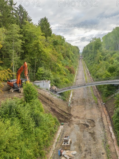 A single excavator during demolition work on a bridge section, next to a straight forest road, bridge demolition, Calw, Germany