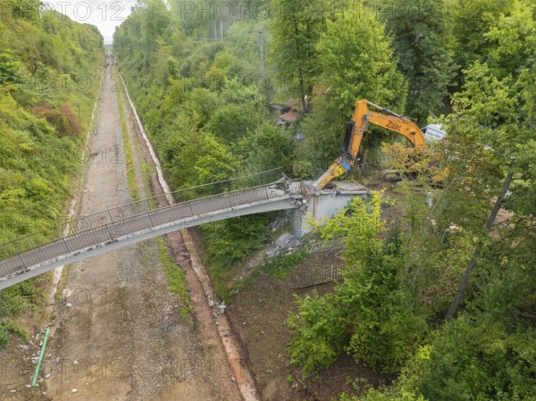 Bird's eye view of an excavator demolishing a bridge in the middle of the forest, with an empty road below, bridge demolition, Calw, Germany