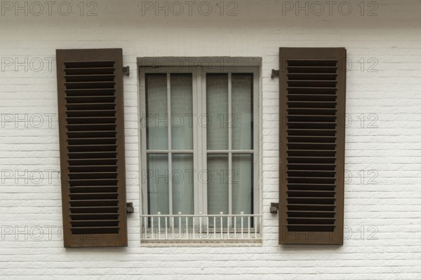 Borken, NRW, Germany, Brown shutters are closed over a window with a white security bar on a white brick wall