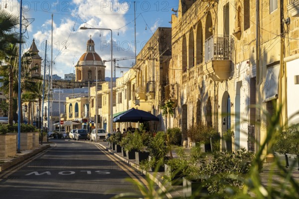 Charming street with limestone building and Saint Mary church at the end, fisherman village of Marsaxlokk, Malta