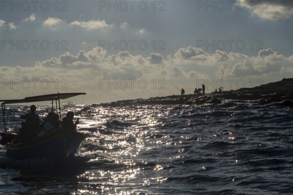 Fishermen on the coast and boat with tourists next to Marsaxlokk, southern part of Malta