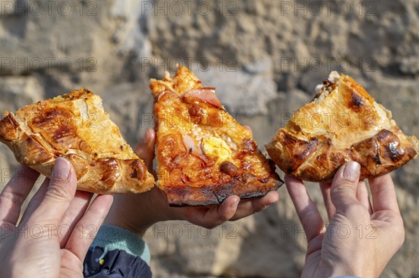 Three slices of maltese pizza hold in the hands of mother and son with stone background, Gozo, Malta