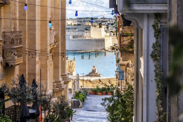 Charming downhill street illuminated with colorful bulbs in Valletta, Malta. St Angelo Fortress in the background