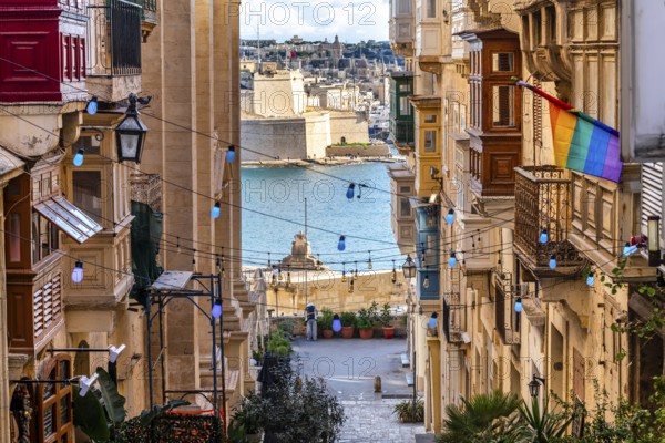 Charming downhill street illuminated with colorful bulbs in Valletta, Malta. St Angelo Fortress in the background