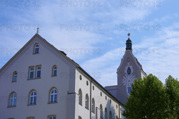 Baroque church and building with bright sky and green tree in the foreground, Regensburg, Bavaria, Germany