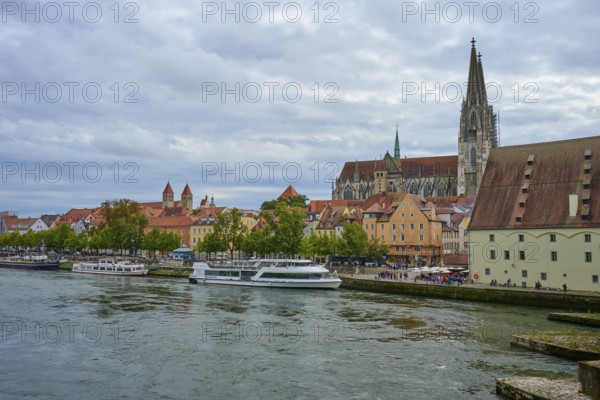 View of a cathedral and boats on a riverbank on a slightly cloudy day, Danube, Regensburg, Bavaria, Germany