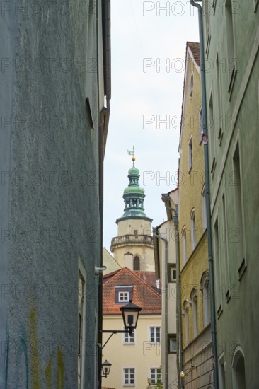 View through a narrow alley to a church tower with surrounding houses, Regensburg, Bavaria, Germany