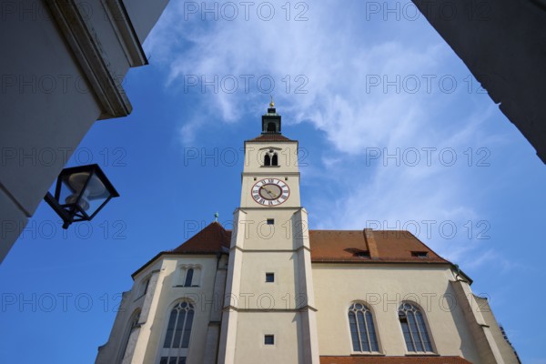 View of a high church tower with a clock under a bright blue sky, flanked by buildings, Neupfarrkirche, Regensburg, Bavaria, Germany