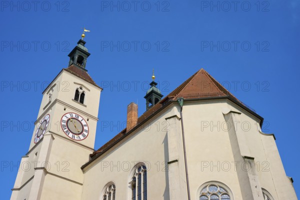 Close-up of a church tower with clock and red tiled roofs against a deep blue sky, Neupfarrkirche, Regensburg, Bavaria, Germany