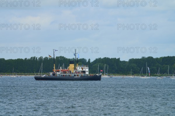 Icebreaker Stettin on a calm sea with several sailing boats and a cloudy sky, Windjammer Parade Kiel 2025, Heikendorf, Kreis Plön, Kieler Förde, Schleswig-Holstein, Germany