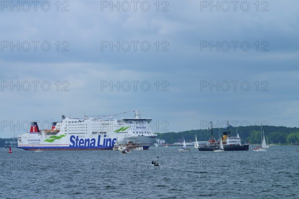 Stena Line ferry and historic ship in a sea travelled by sailing boats with cloudy sky, Windjammer Parade Kiel 2025, Heikendorf, Kreis Plön, Kieler Förde, Schleswig-Holstein, Germany
