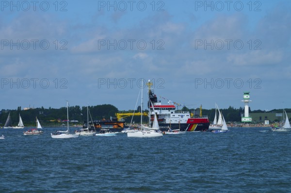 Large ship Arkona Coast Guard and numerous smaller sailing boats in the water in front of a lighthouse Friedrichsort, Windjammer Parade Kiel 2025, district Plön, Kiel Fjord, Schleswig-Holstein, Germany