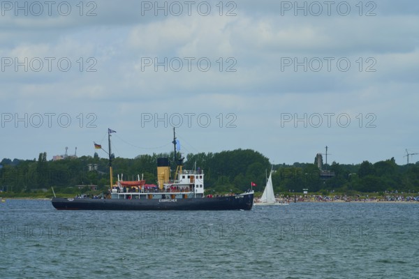 Historic icebreaker Stettin and a small sailing boat in front of a green coastal landscape and cloudy sky, Windjammer Parade Kiel 2025, Heikendorf, Plön district, Kiel Fjord, Schleswig-Holstein, Germany